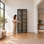 Furnilora 2 Door Storage Cabinet, full-height doors and smoke-grey glazing, with a woman standing beside the cabinet.