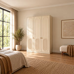 Kapilosa 3 Door Wooden Wardrobe, detailed with small brass-tone handles and arched panel detailing in a sunlit bedroom.