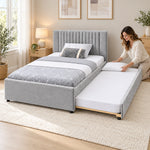 Sillavony Light Grey Kids Trundle Bed, light grey upholstery and small dark feet, beside a woman making the pull-out bed.