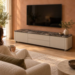 Vicindola Marble Top TV Unit, rounded corners and short recessed feet, beside a woman in a sunlit furnished living room.