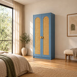 Webinora Blue 2 Door Wooden Cane Wardrobe pairs arched woven panels with a narrow cabinet body beside a bedroom window.