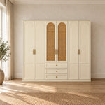 Wratinora 6 Door Wooden Wardrobe with Drawers, showing brass-tone pulls and three lower drawers beside a bedroom window.