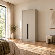 Balomora 2 Door Wooden Wardrobe displays long black handles together with a neutral outer case beside a bedroom window.