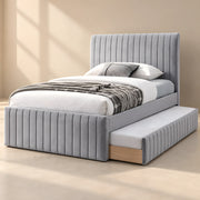 Bexylona Grey Kids Trundle Bed, showing channelled grey upholstery and wood-tone underbed trim beside a bedroom window.