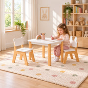 Costzony White Kids Table with 2 Chairs: a white square tabletop beside a child seated at the table on a patterned rug.