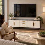 Crimpedy Black Marble Top TV Unit, a dark marble top and gold-tone handles, beneath a wall-mounted TV with a woman nearby.