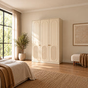 Kapilosa 3 Door Wooden Wardrobe, detailed with small brass-tone handles and arched panel detailing in a sunlit bedroom.
