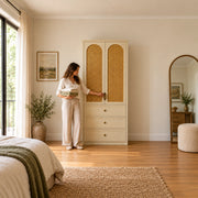 Mossylora Cane Cabinet Storage with Three Drawers beside a woman reaching toward the door, featuring woven cane inserts.