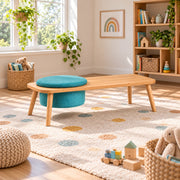 Stepsoly Kids Wooden Floor Table with Pouf pairs a round teal pouf with four splayed wood legs beside a playroom window.