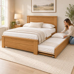Zikroniya Wooden Kids Trundle Bed beside a woman making the pull-out bed; square wooden posts and projecting top rails.